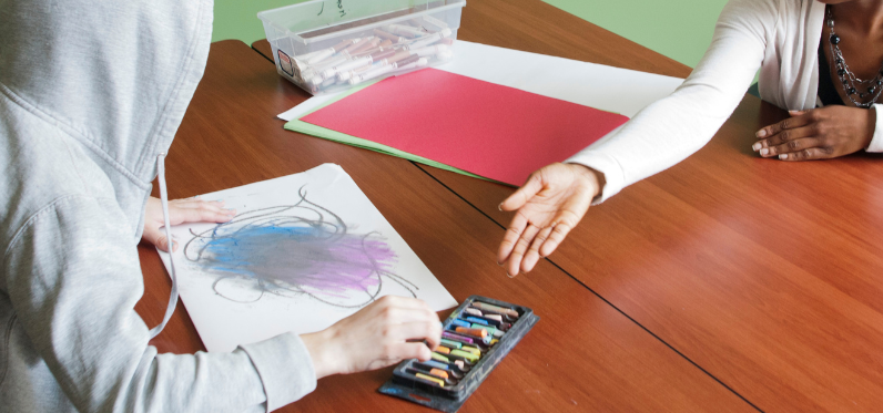 Image of zoomed in pastel chalk with page drawing and hands picking up the chalk
